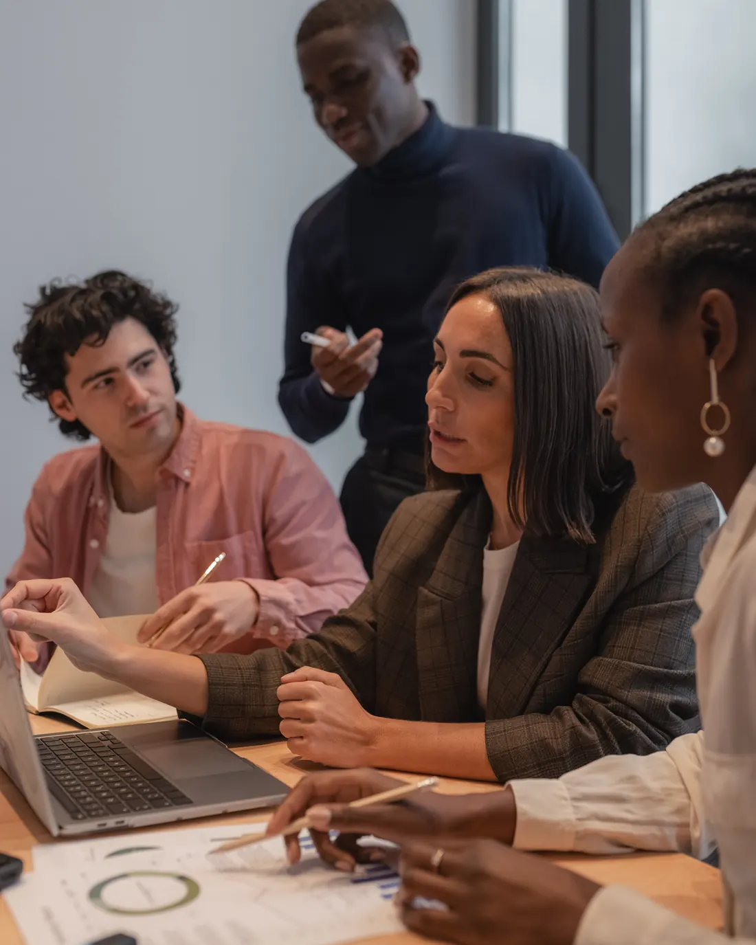 Illustrative photograph: four people around a laptop and printed reports; one person stands while another points toward the screen.